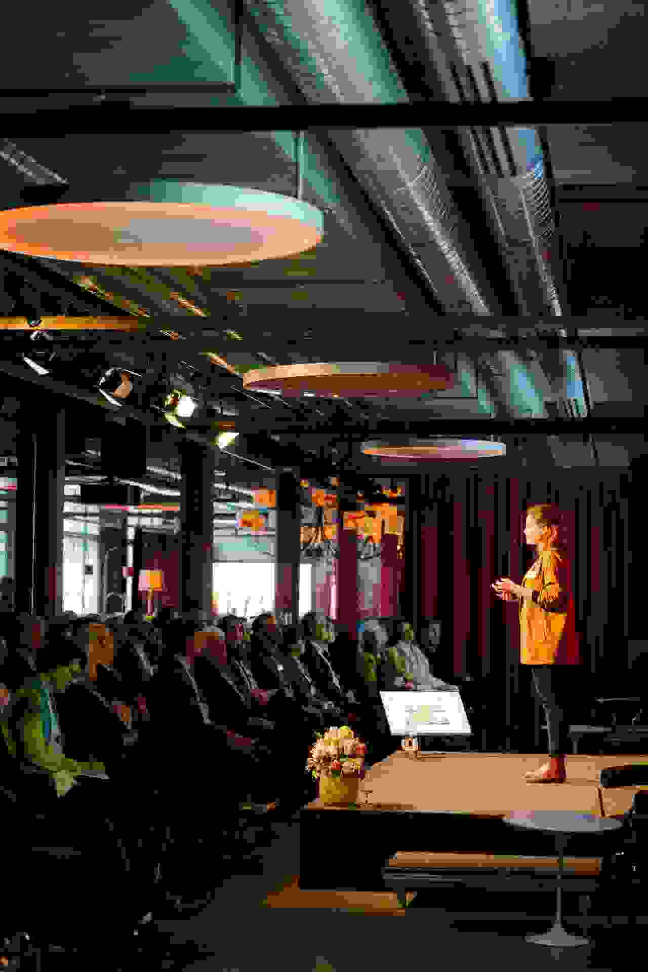 Papiersaal stage with presentation/conference, woman speaks, people sit 